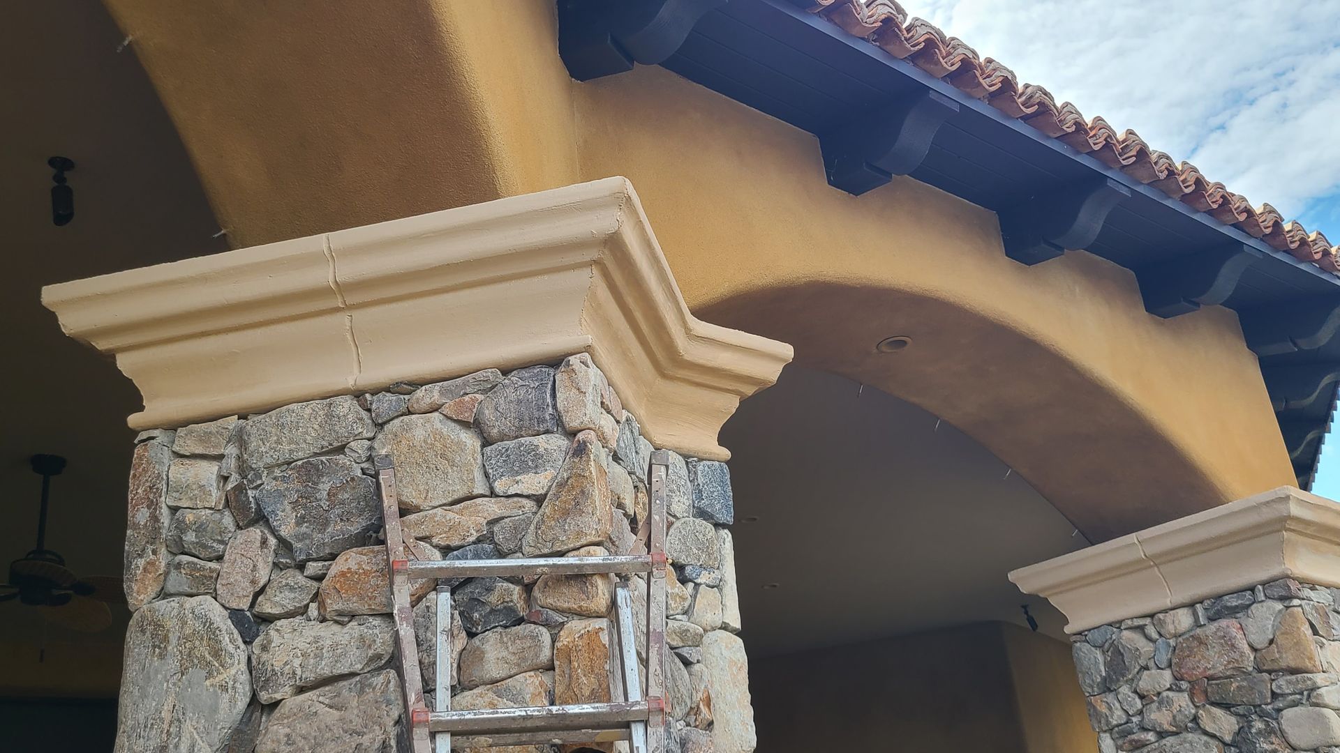 Stone pillars supporting a tan archway, with a dark wood overhang and blue sky visible.