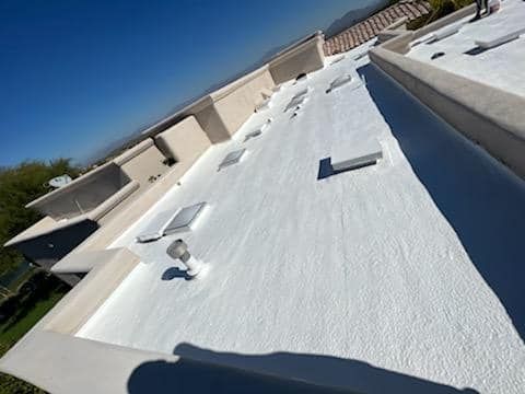 White coated flat roof with skylights and vents on a sunny day.