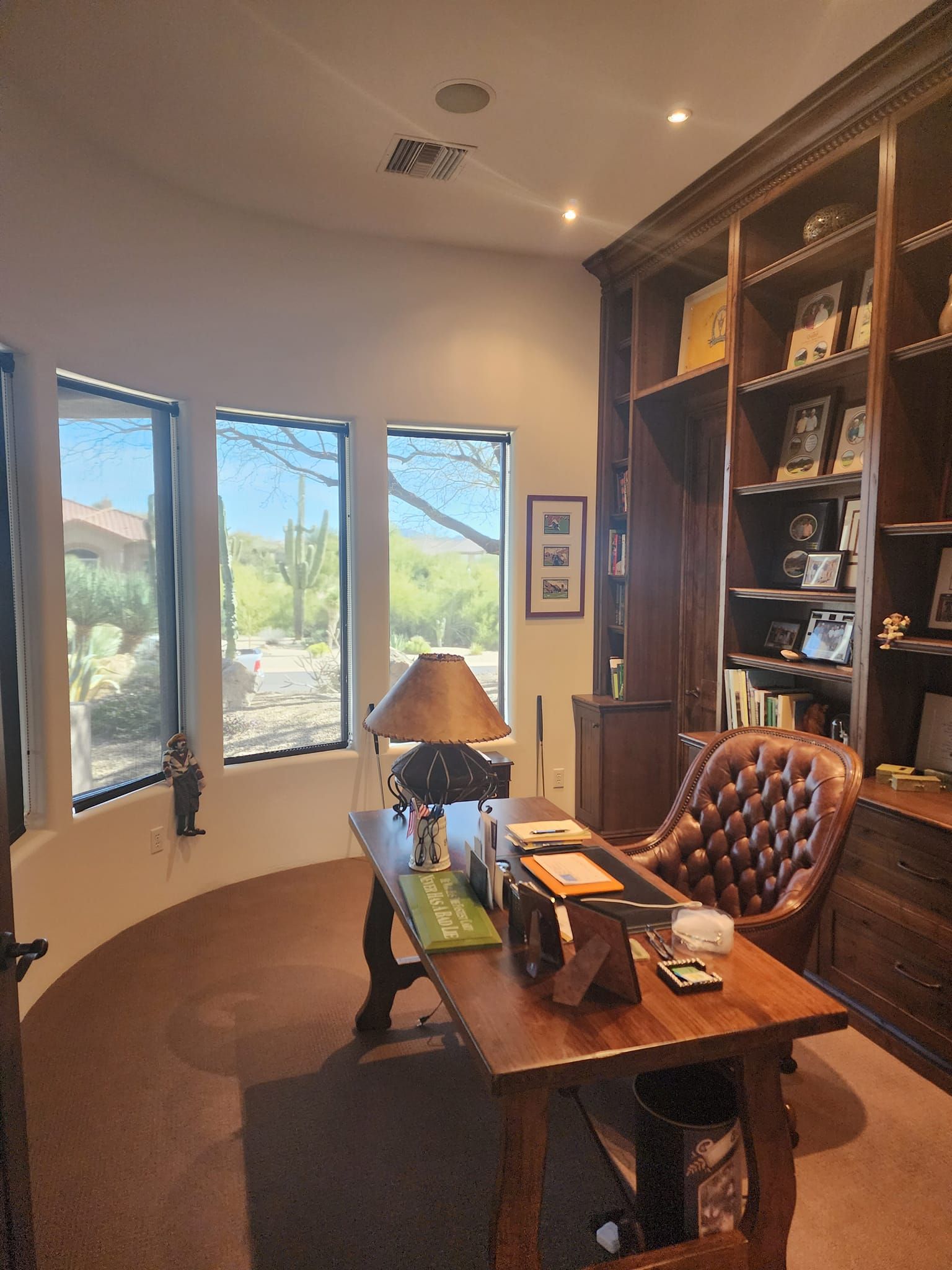 Office with large wooden desk, leather chair, bookshelves, and windows overlooking desert landscape.