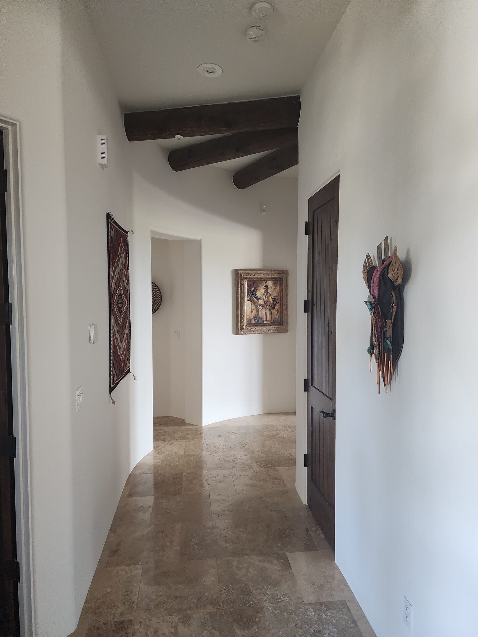 Hallway with textured stone floor, white walls, dark wooden beams and door. Art pieces on the walls.