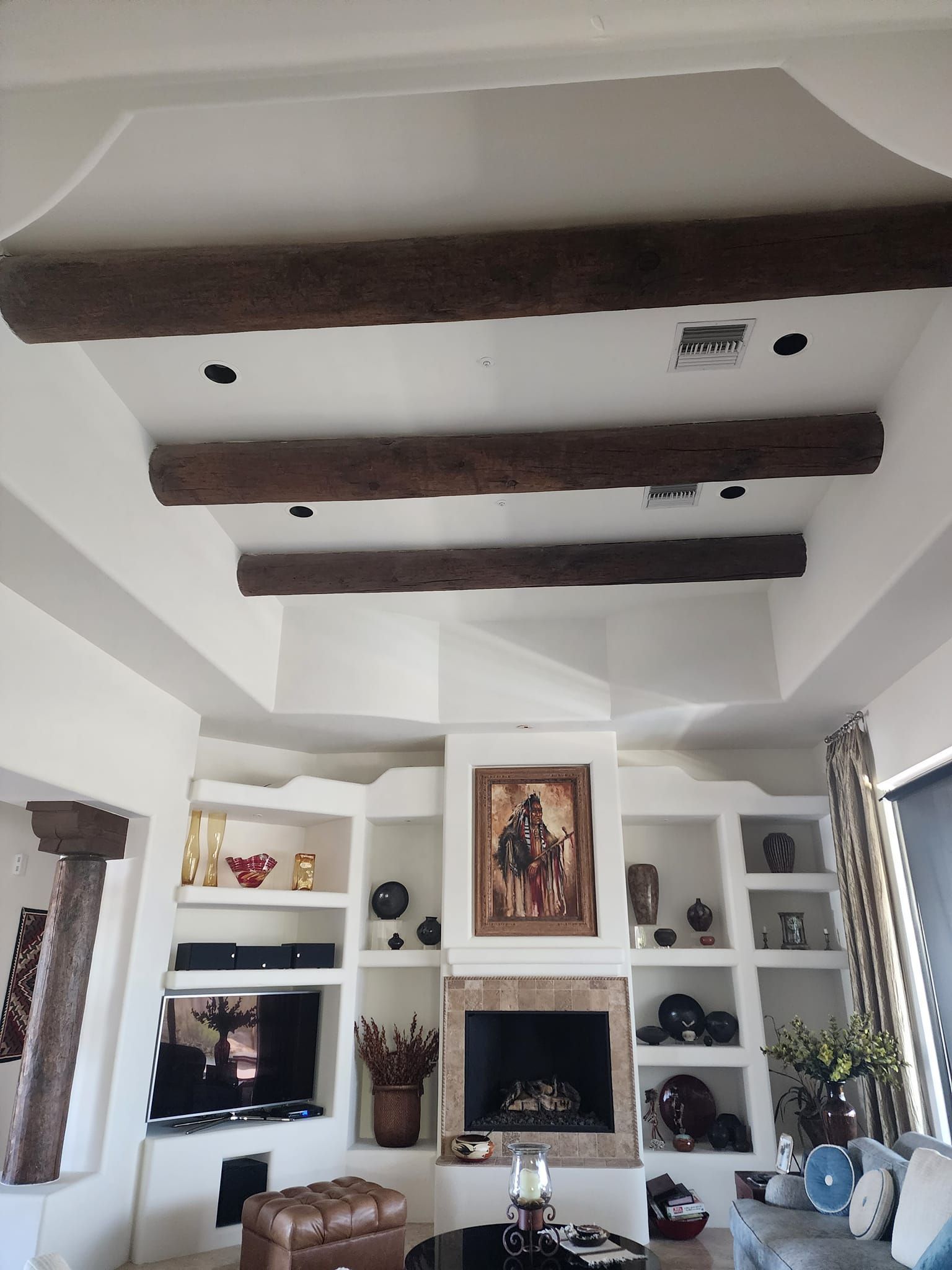 Living room interior with built-in shelves, fireplace, brown ceiling beams, and recessed lighting.