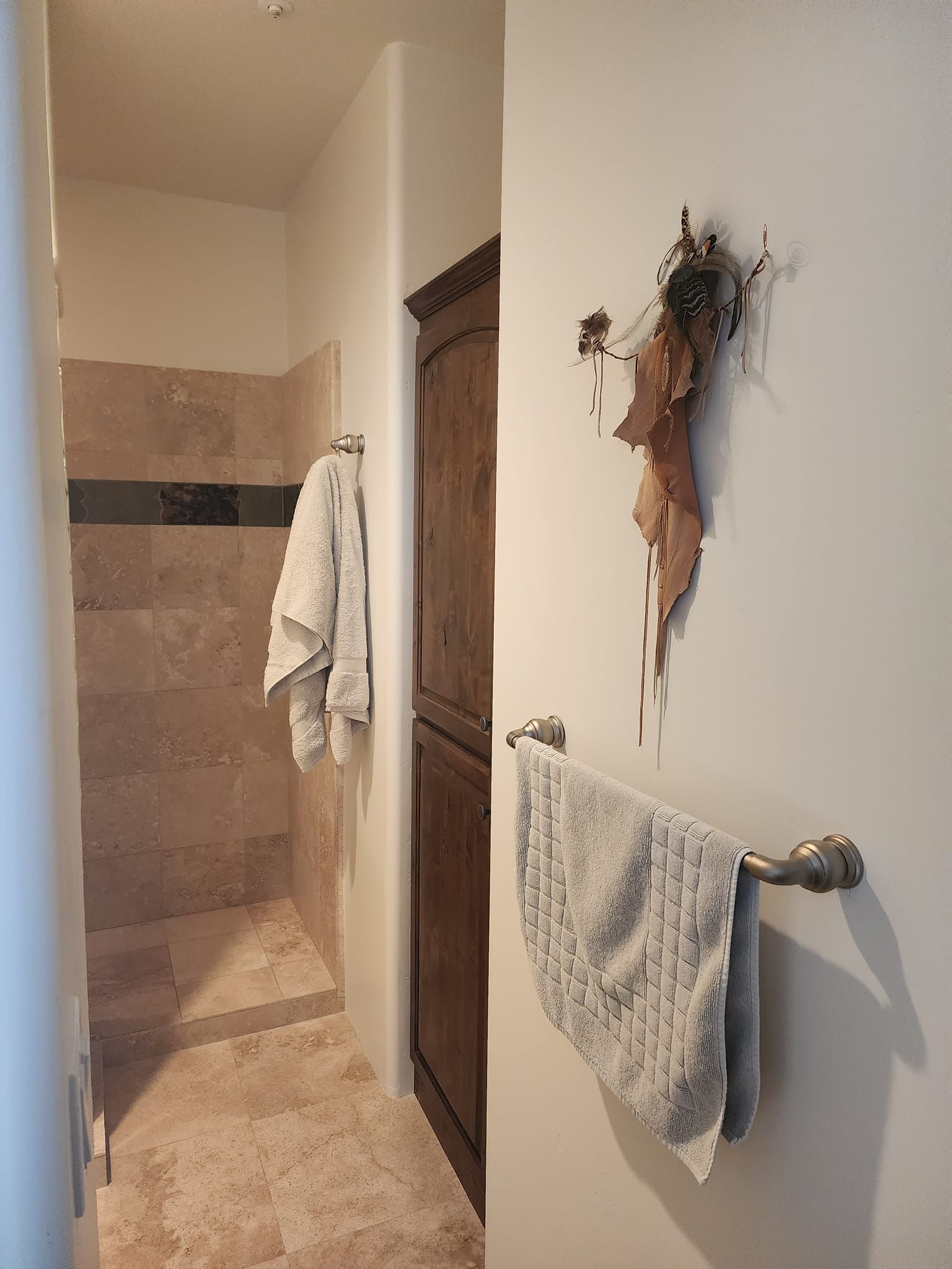 Narrow bathroom with shower, brown stone walls, wooden cabinet, and towels on a rack.