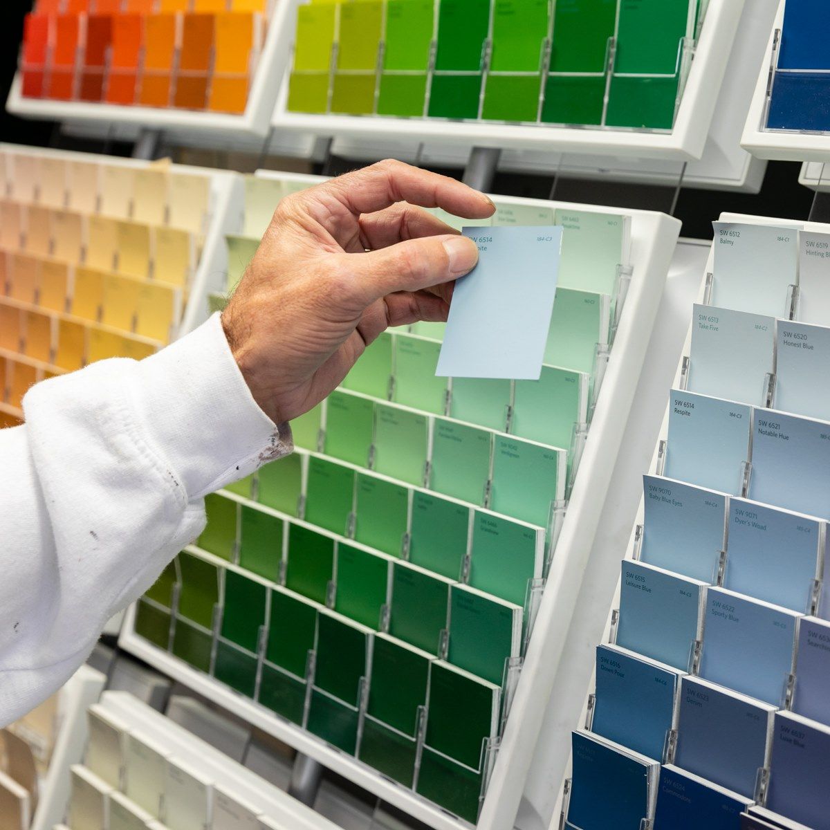 Person holding a light blue paint swatch, comparing it to other colors in a display.