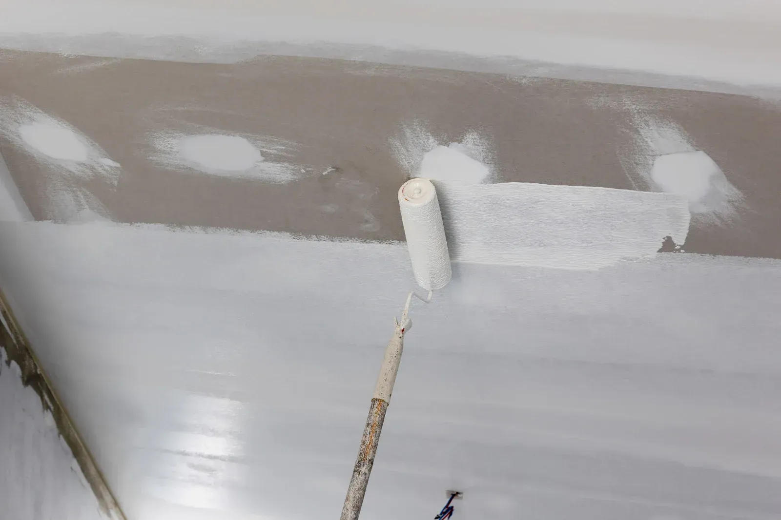 A person using a paint roller to apply white paint to a ceiling.