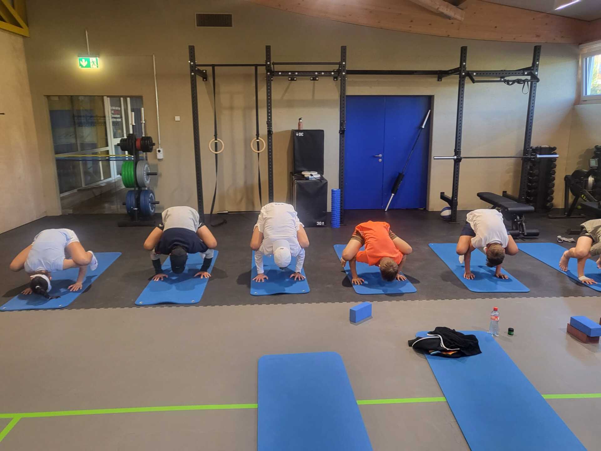 Eine Gruppe von Menschen macht in einem Fitnessstudio Yoga auf blauen Matten.