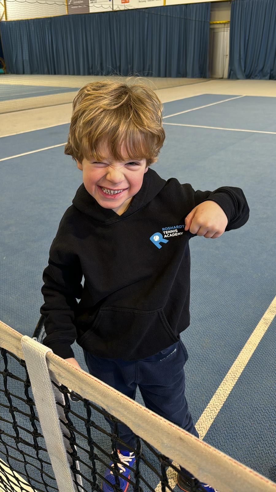Ein kleiner Junge steht neben einem Tennisnetz auf einem Tennisplatz.