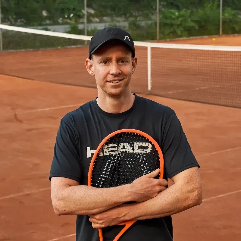 Ein Mann in einem roten Hemd hält einen Tennisschläger