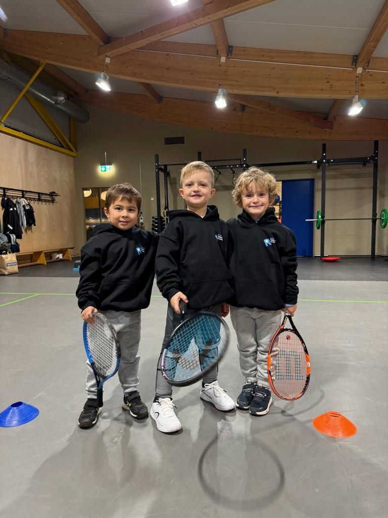 Drei junge Jungen halten in einer Turnhalle Tennisschläger.
