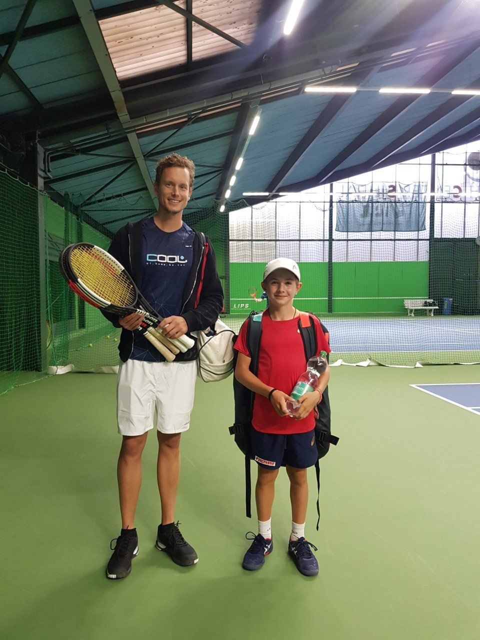 Ein Mann und ein Junge stehen mit Tennisschlägern in den Händen auf einem Tennisplatz.