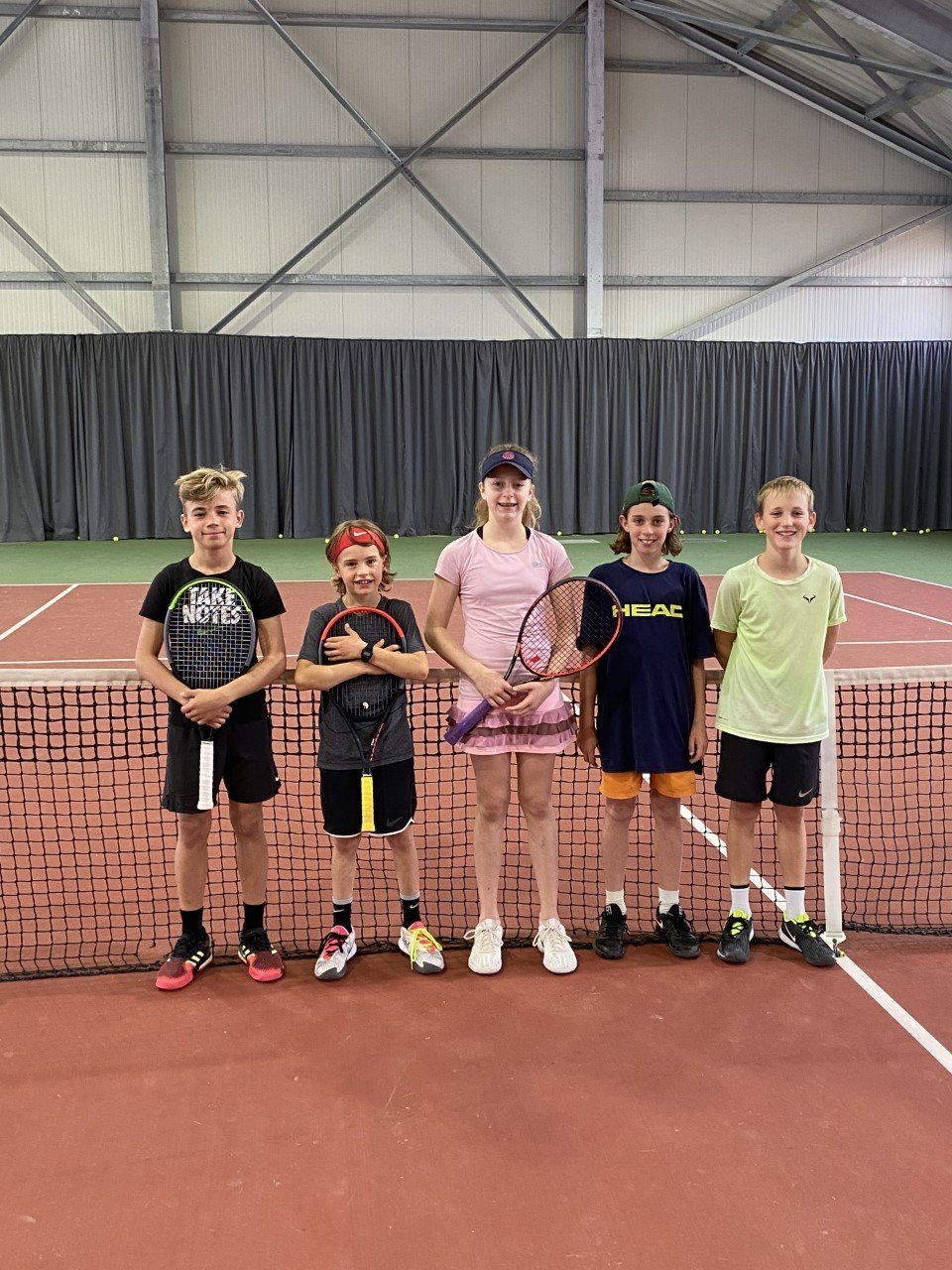 Eine Gruppe Kinder posiert auf einem Tennisplatz für ein Foto.
