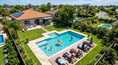 Aerial view of a backyard with a swimming pool, lounge chairs, patio, and a house with solar panels on a sunny day.