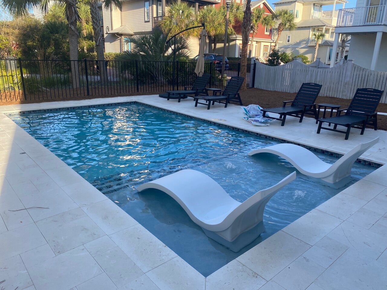 A rectangular swimming pool with two white lounge chairs submerged in a shallow tanning ledge on a sunlit patio.