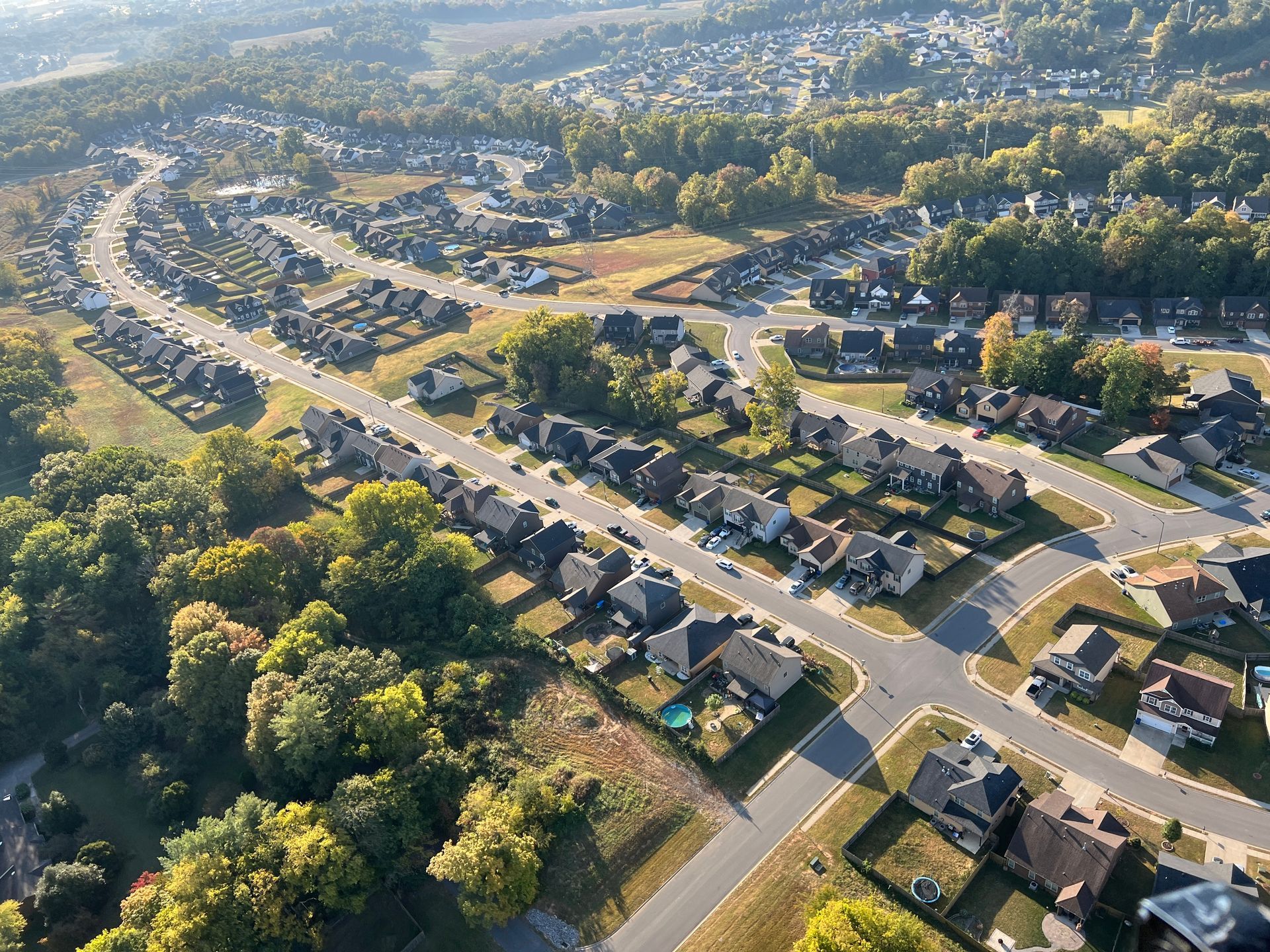 Aerial view of a suburban neighborhood with houses, streets, and trees under a sunny sky.
