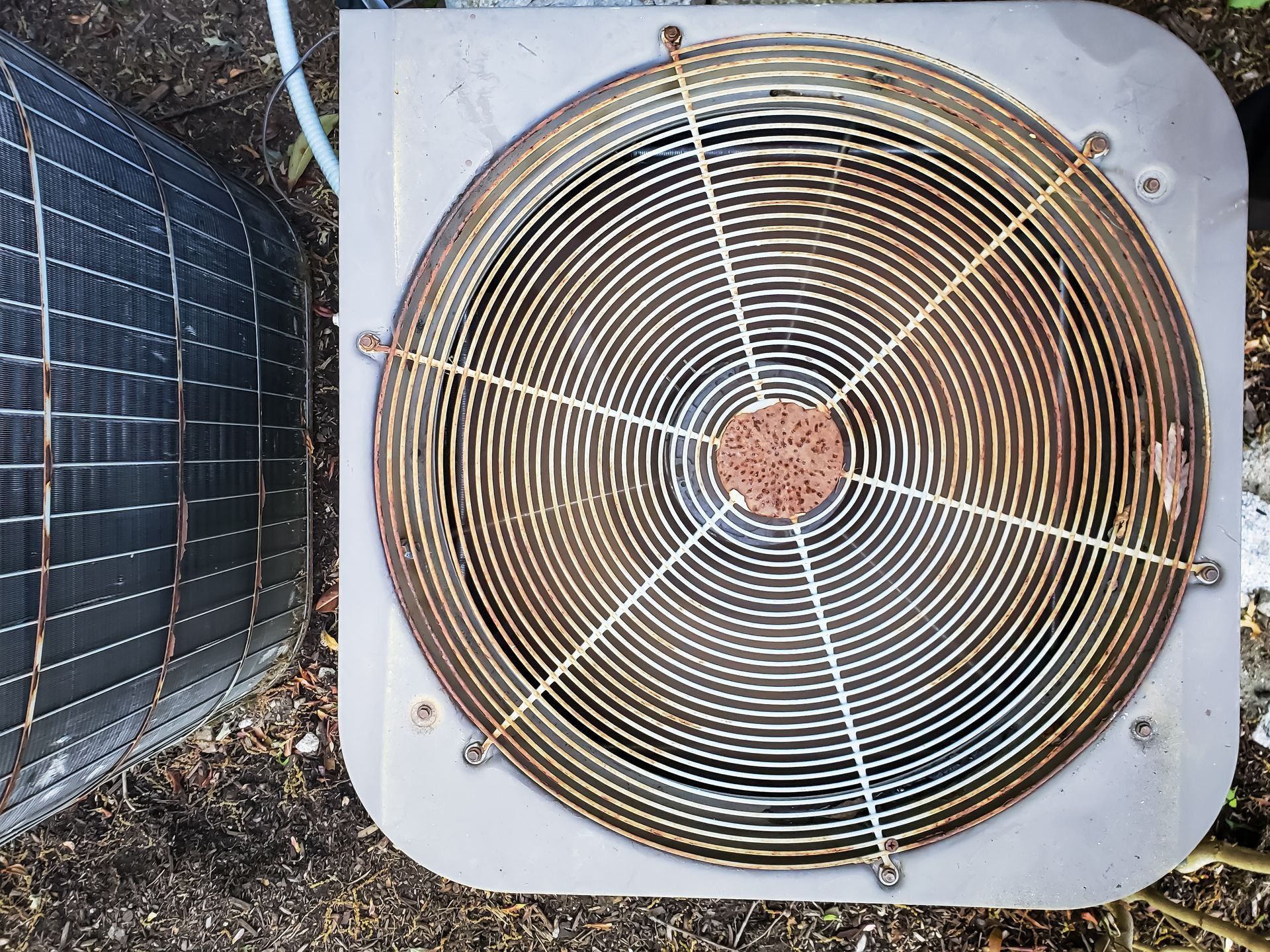 Exterior air conditioning unit, rusty fan guard, rectangular shape.