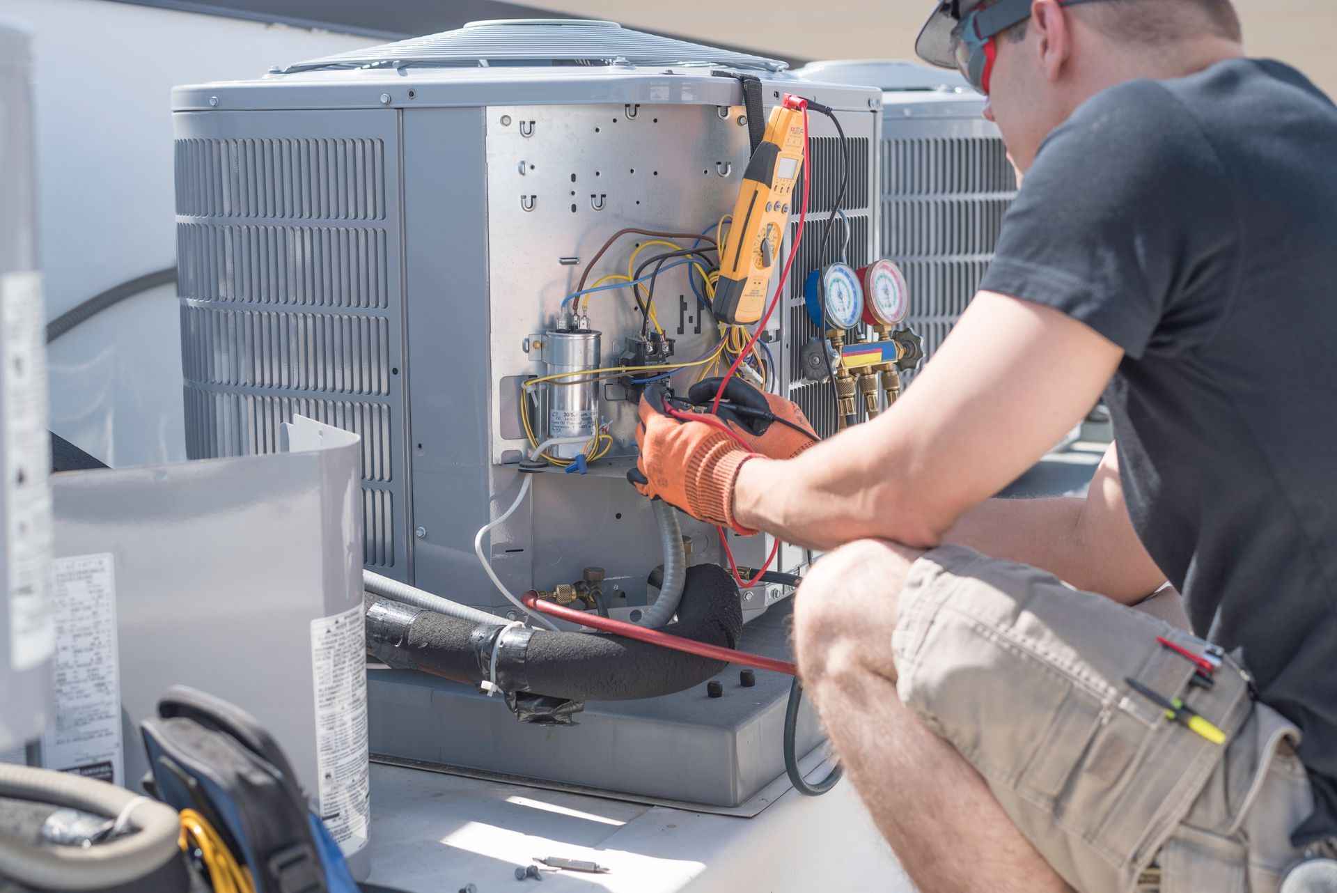 HVAC technician repairing an air conditioning unit on a rooftop, using tools to check components.
