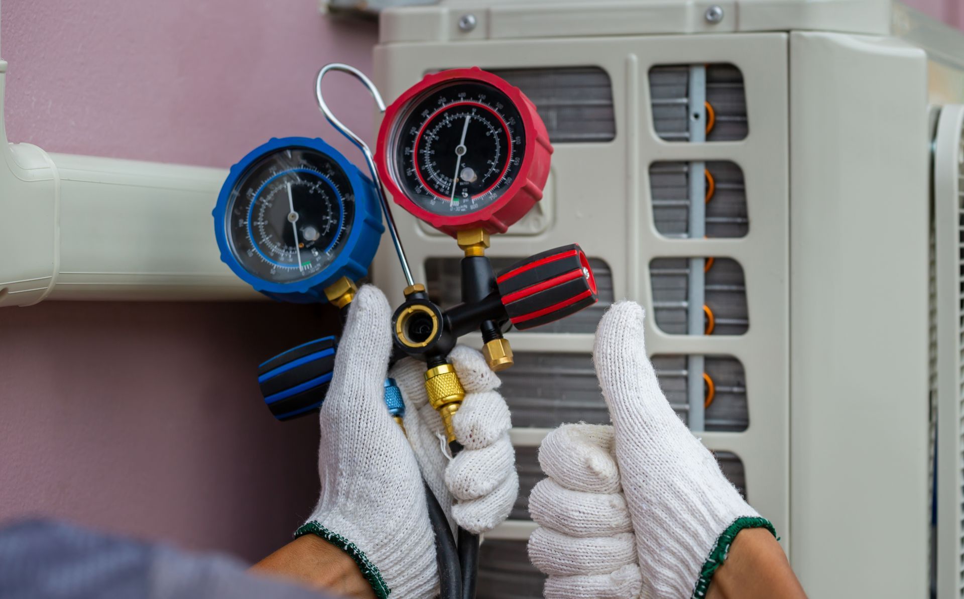 Person wearing gloves giving thumbs-up, using gauges to service an air conditioning unit.