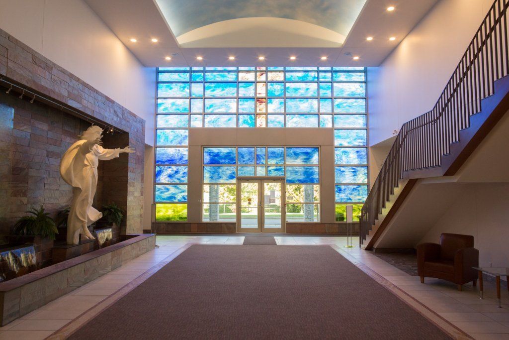 Lobby with a large stained glass window, fountain with statue, and staircase.