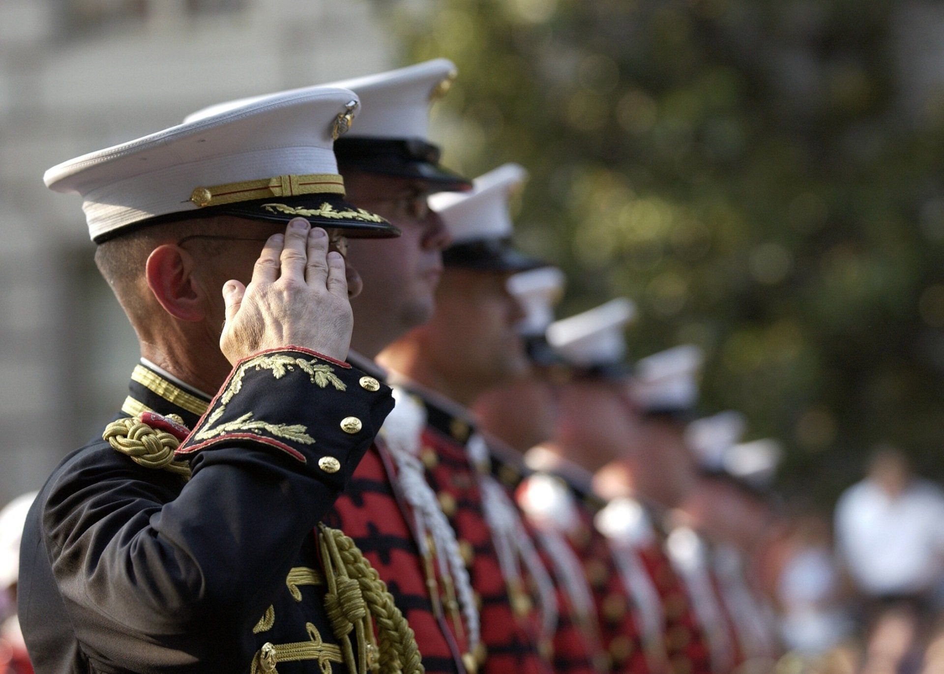 A man in a military uniform salutes in front of a cemetery