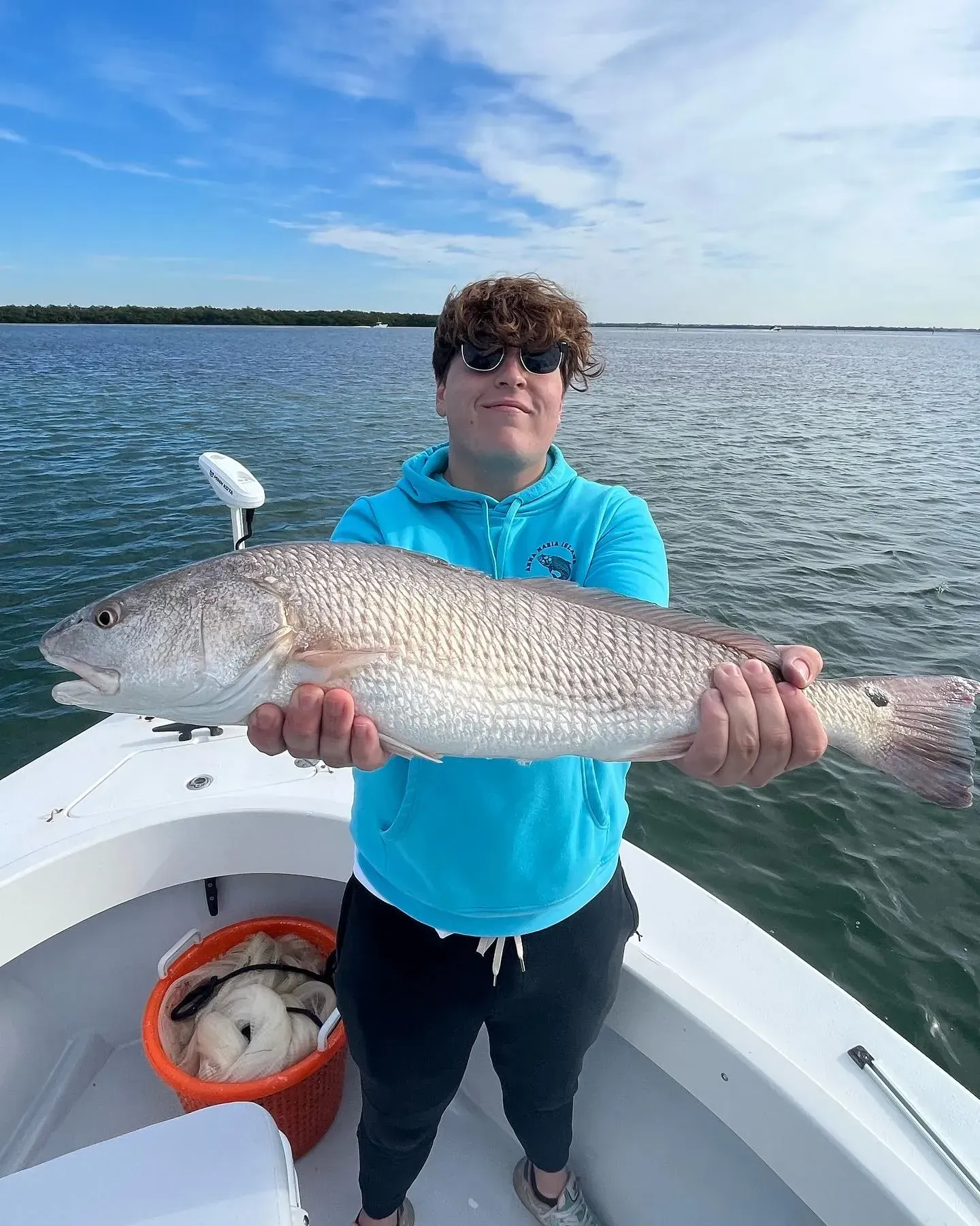 A young man is holding a large fish on a boat.