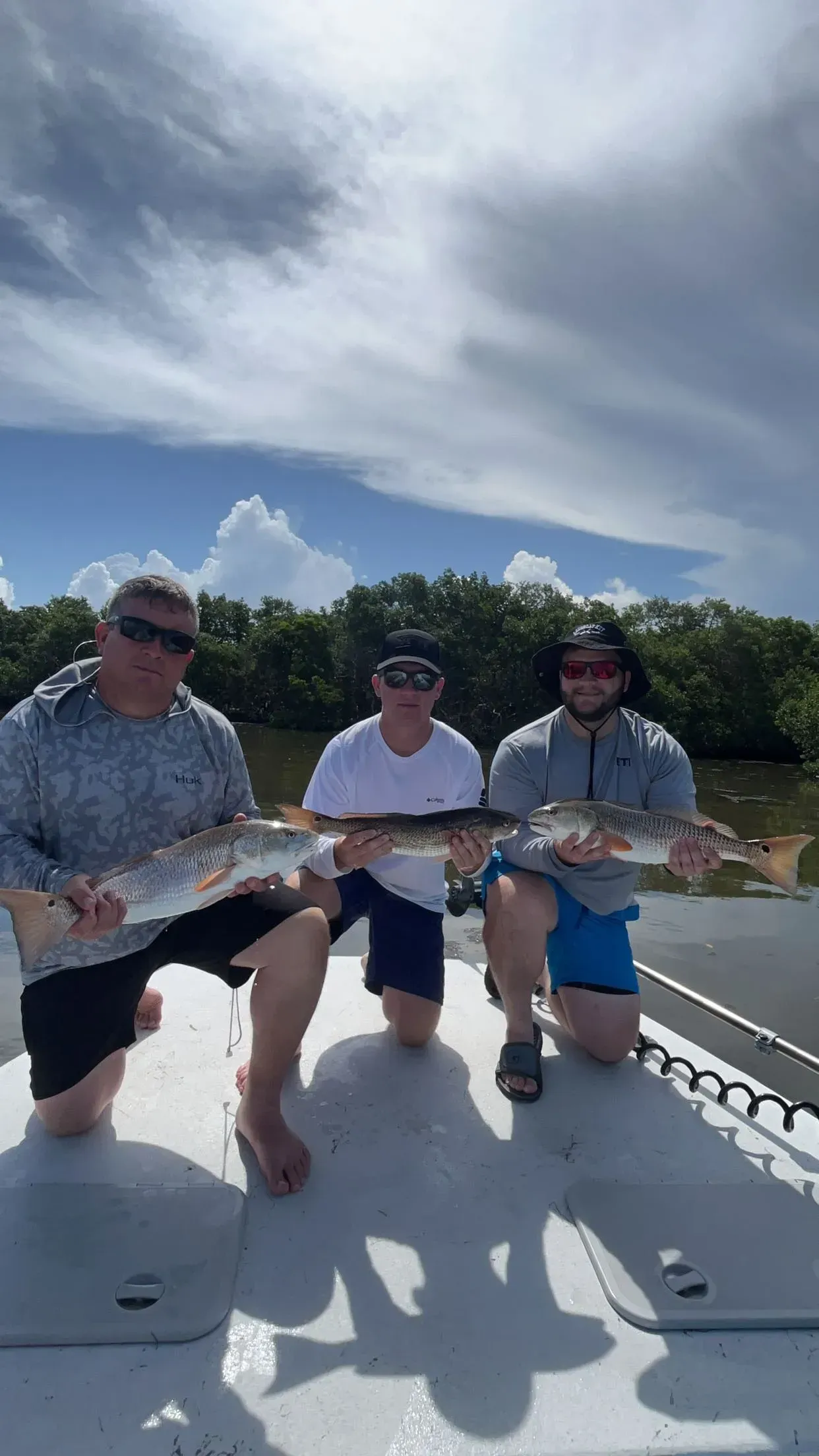 Three men are sitting on a boat holding fish.