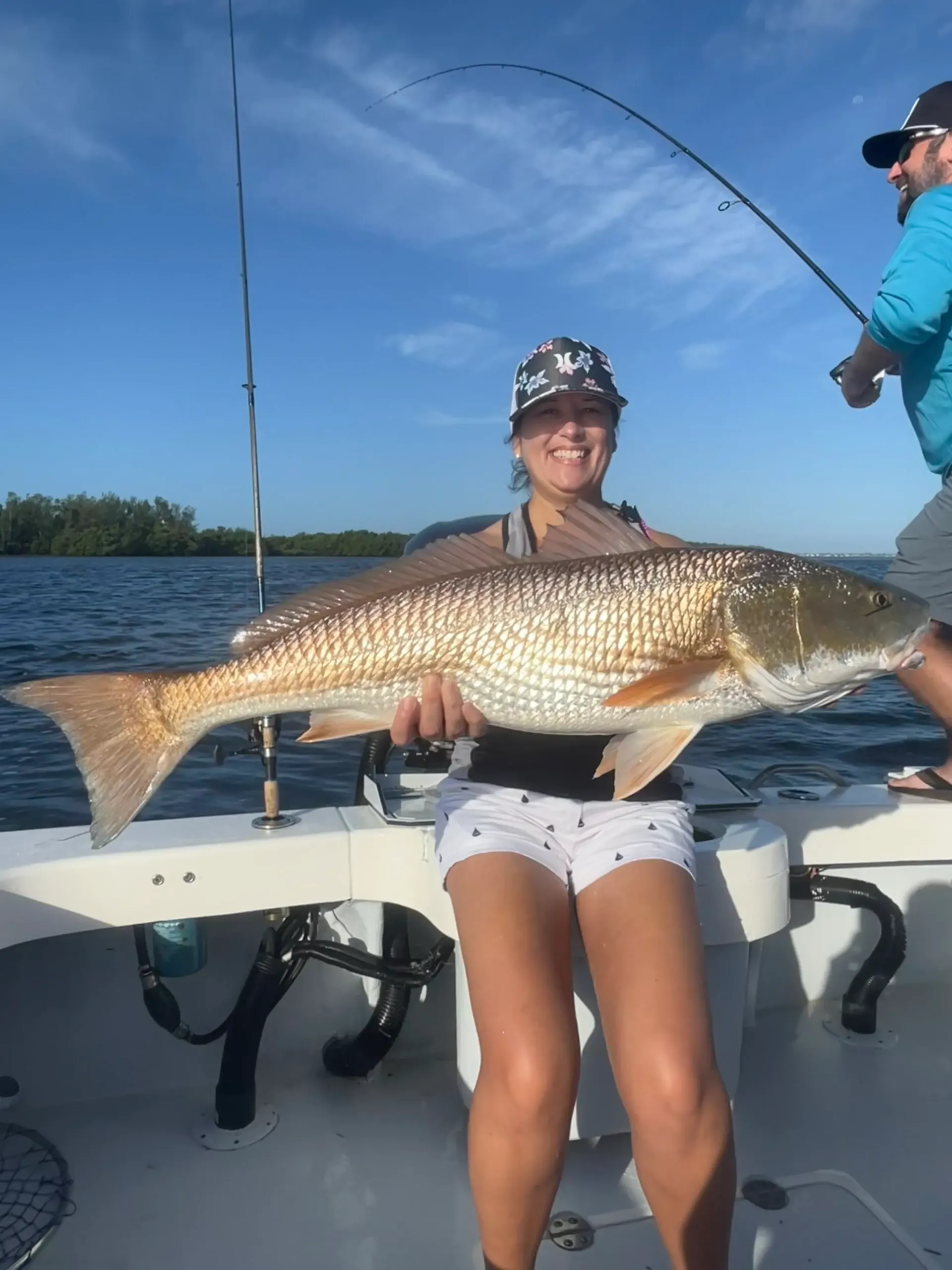 A woman is sitting on a boat holding a large redfish.