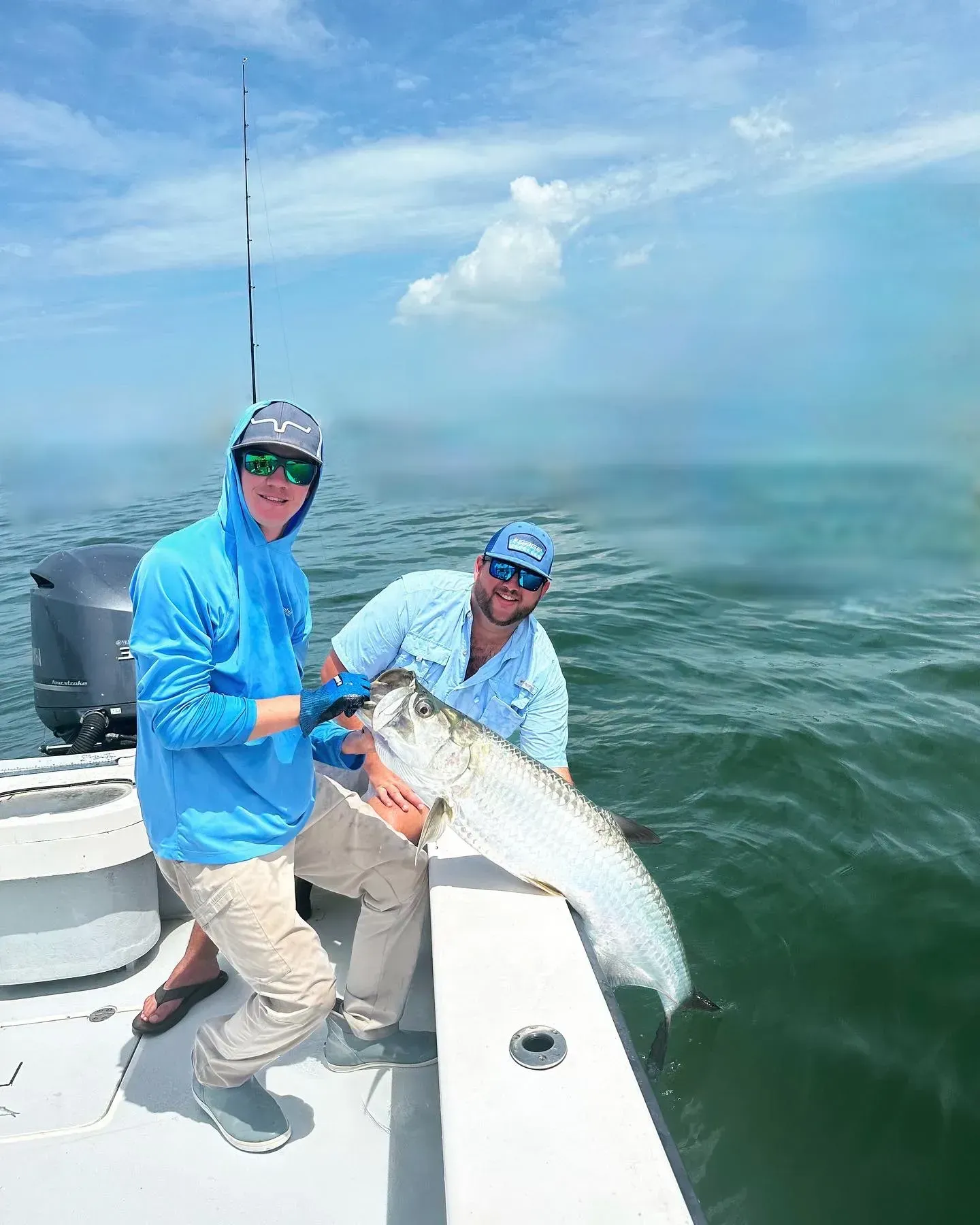 Two men are standing on a boat holding a large fish.