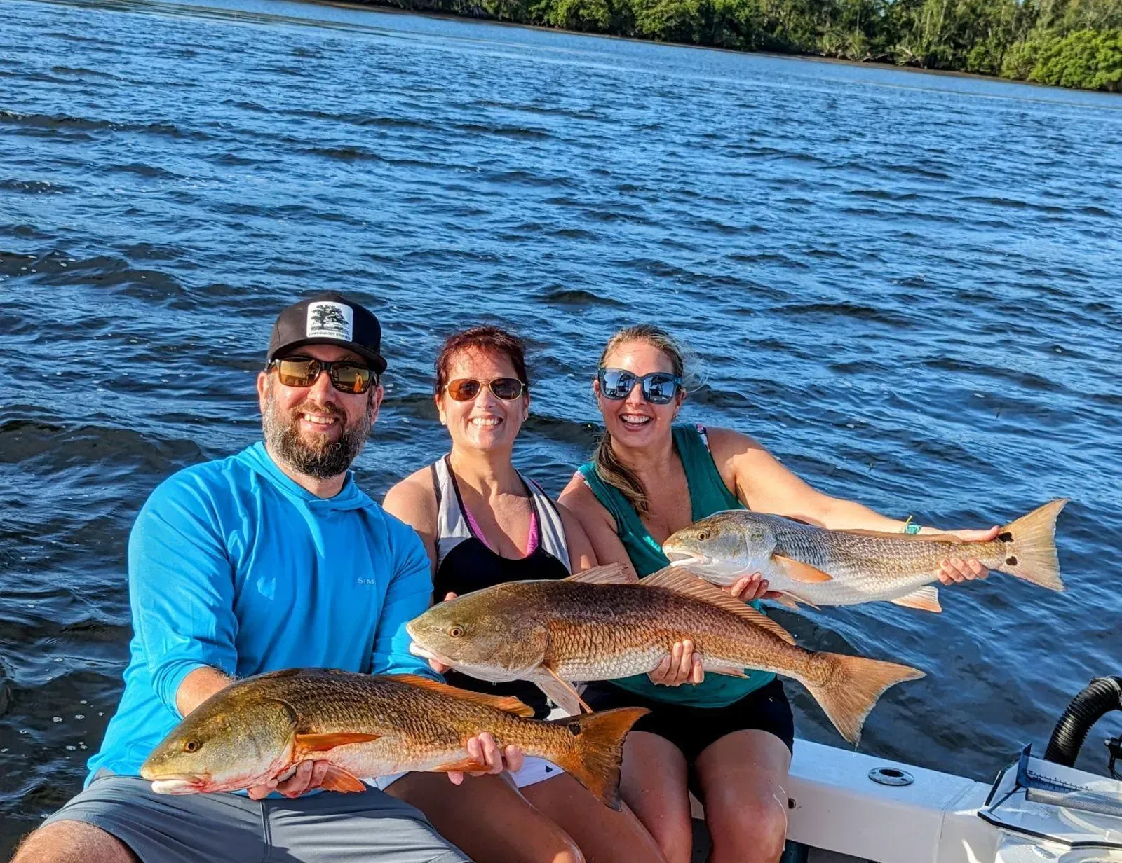 A man and two women are sitting on a boat holding fish.
