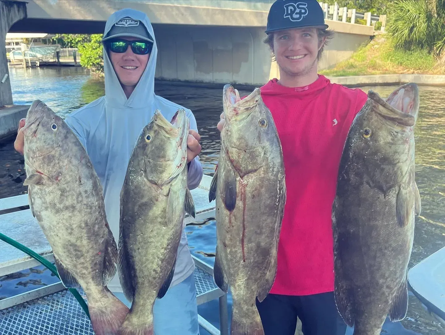 Two young men are holding large fish in their hands on a boat.