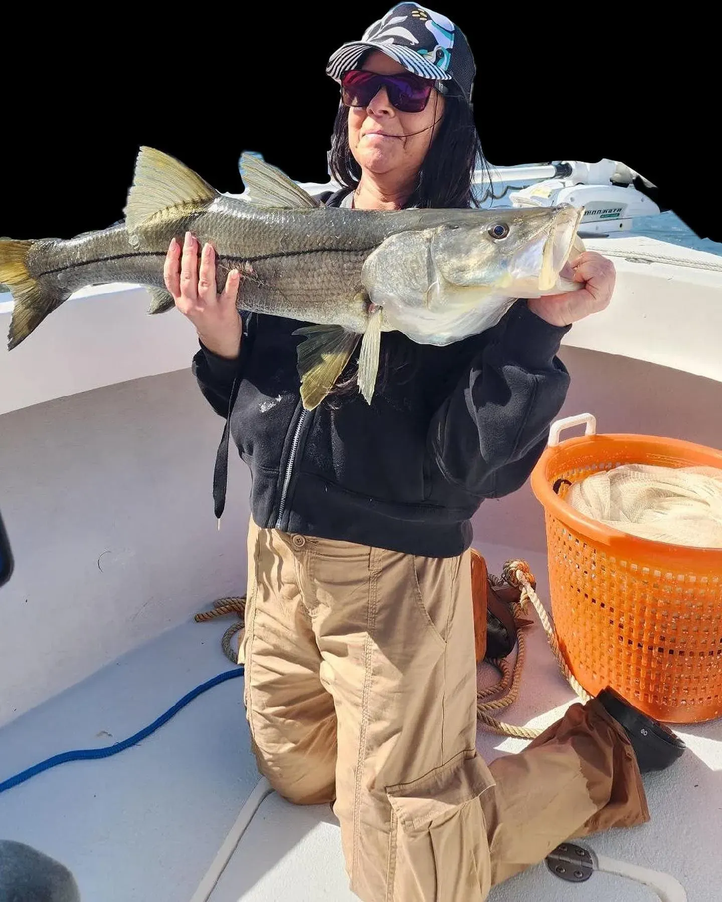A woman is kneeling on a boat holding a large fish.