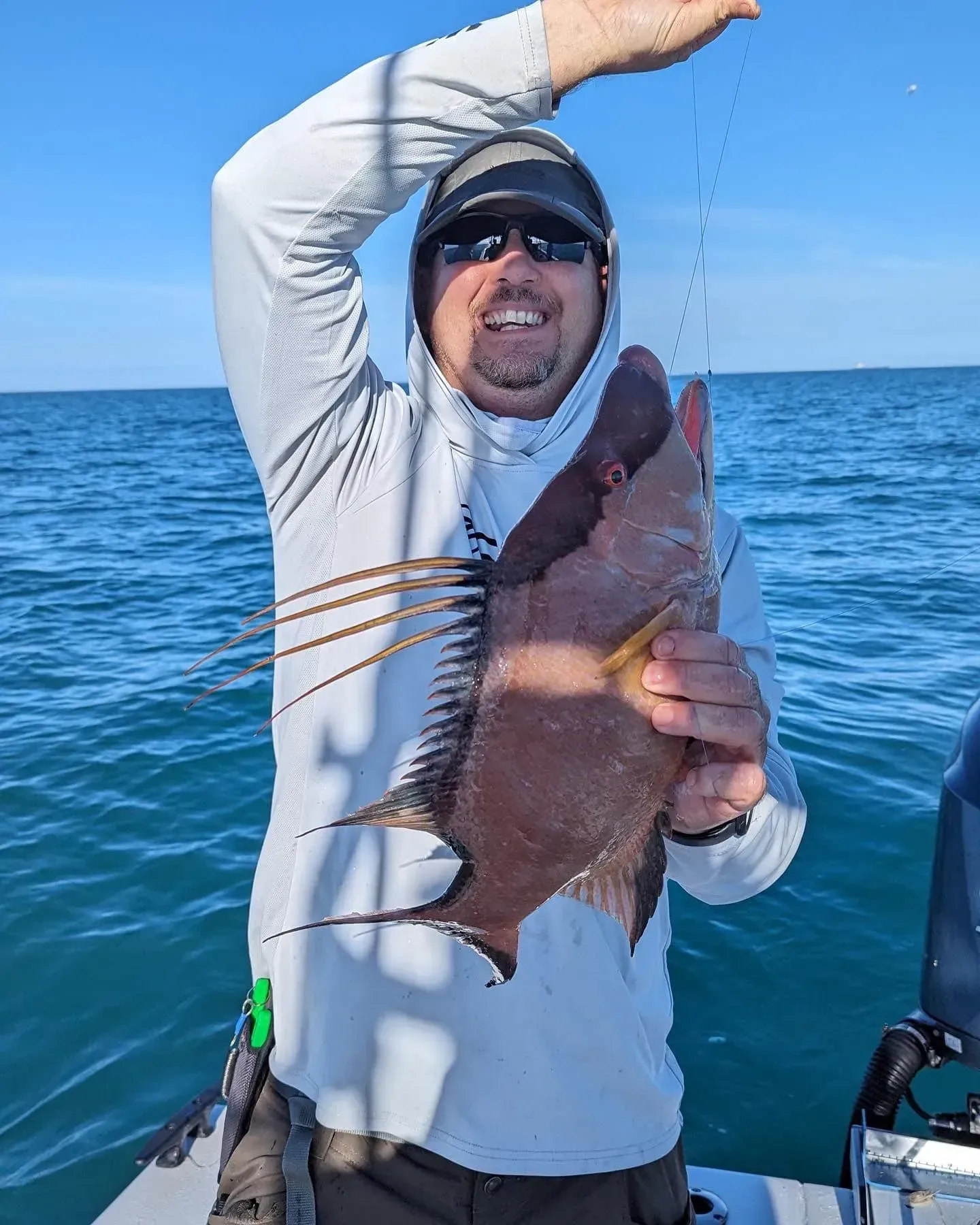 A man is holding a fish on a boat in the ocean.