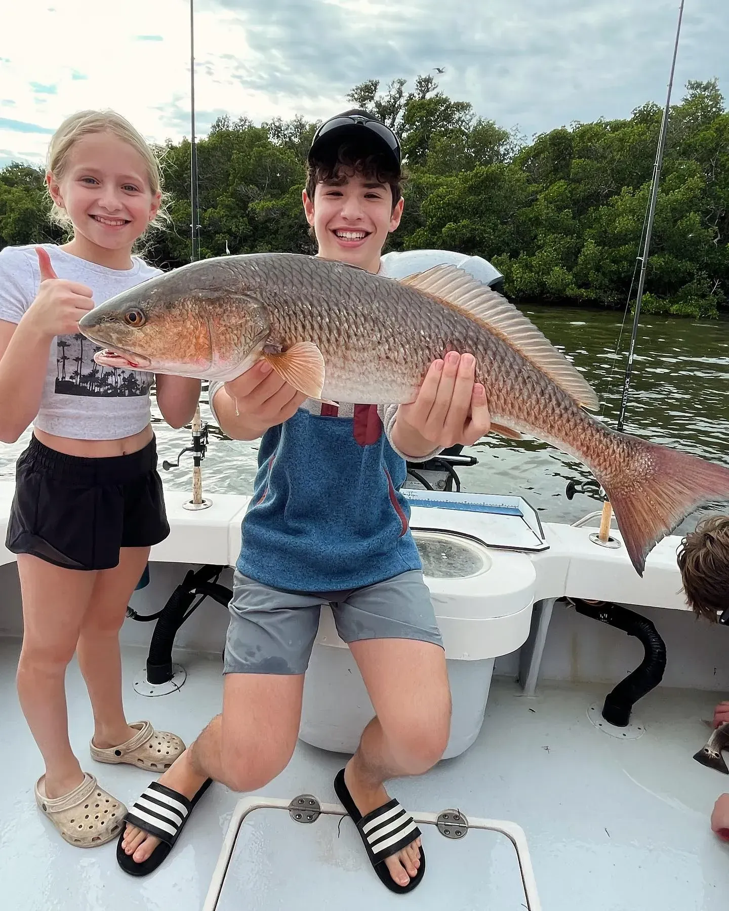 A boy and a girl are holding a large fish on a boat.