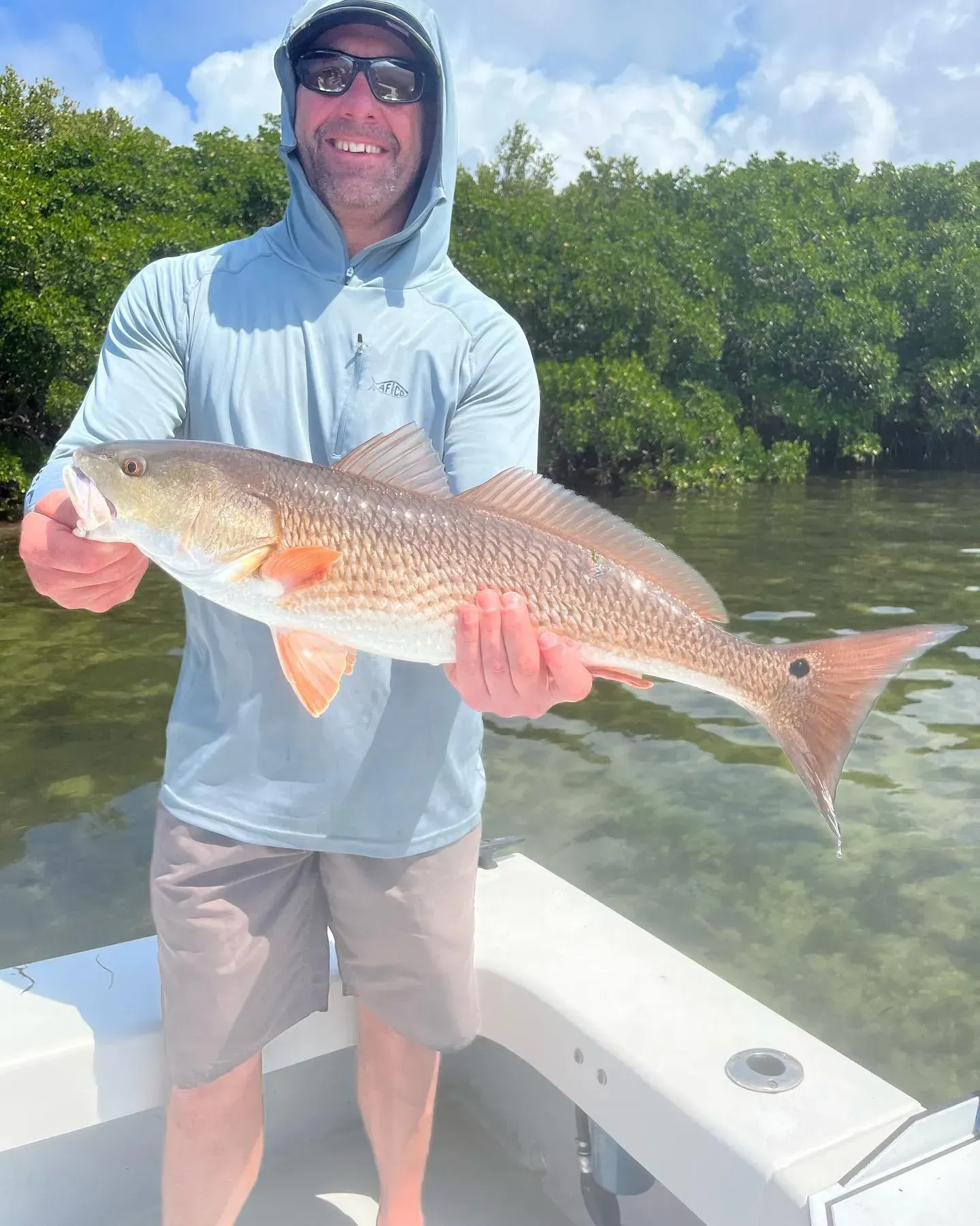 A man is standing on a boat holding a large red fish.