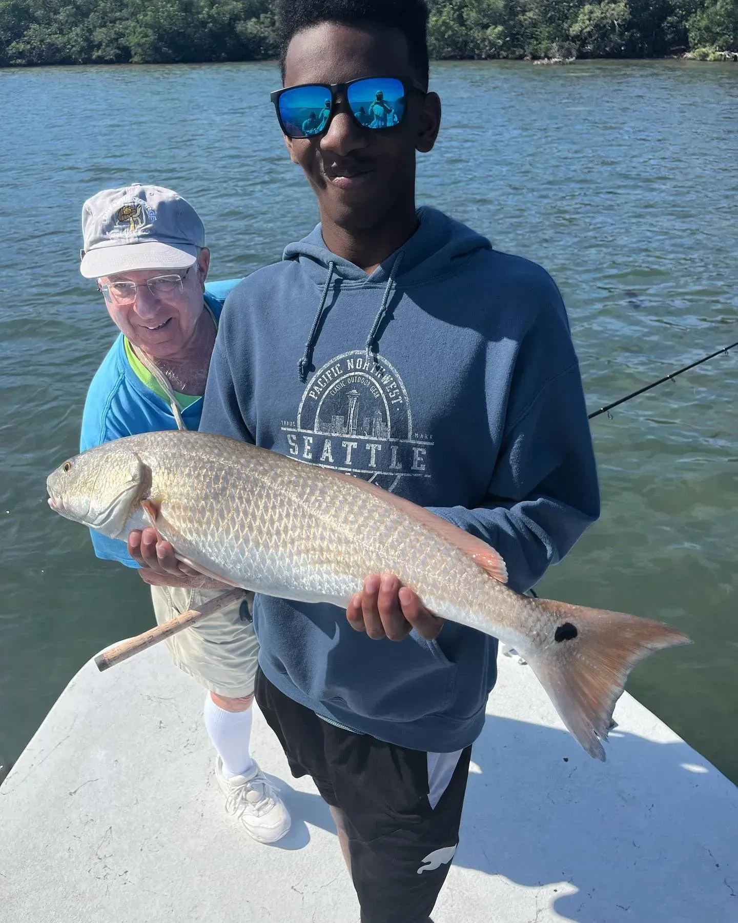A young man is holding a large fish on a boat.