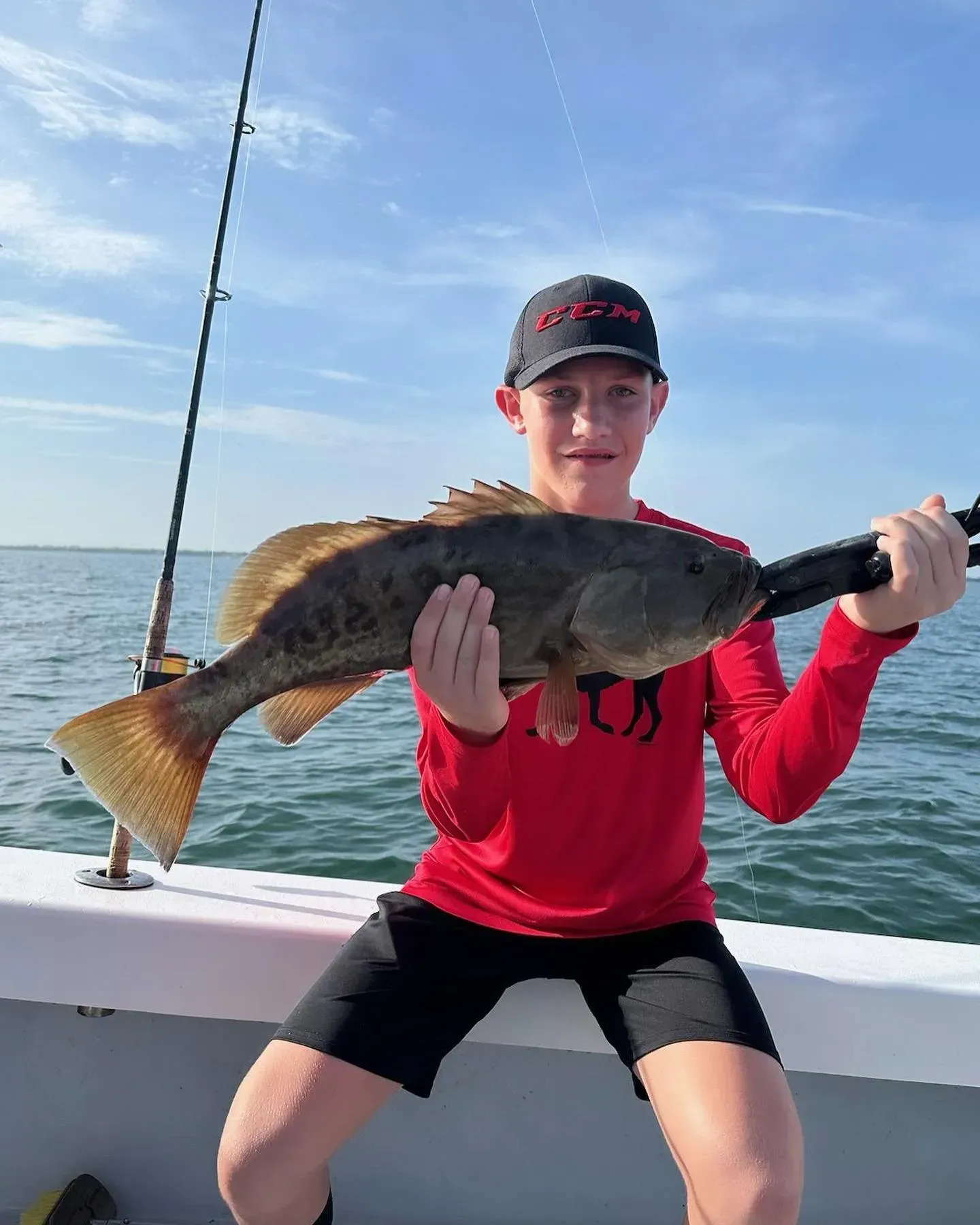 A young boy is sitting on a boat holding a large fish.