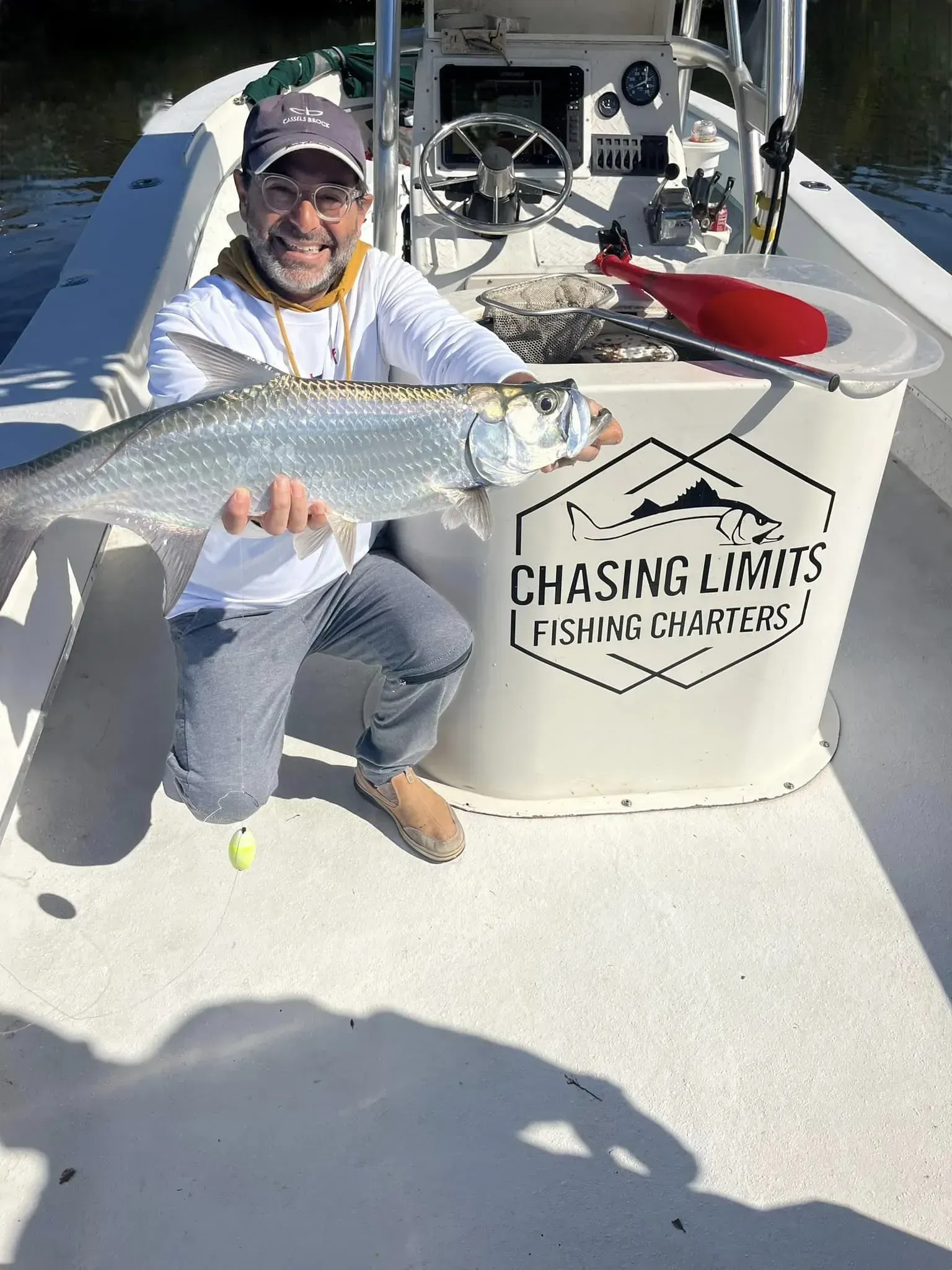 A man is kneeling on a boat holding a large fish.
