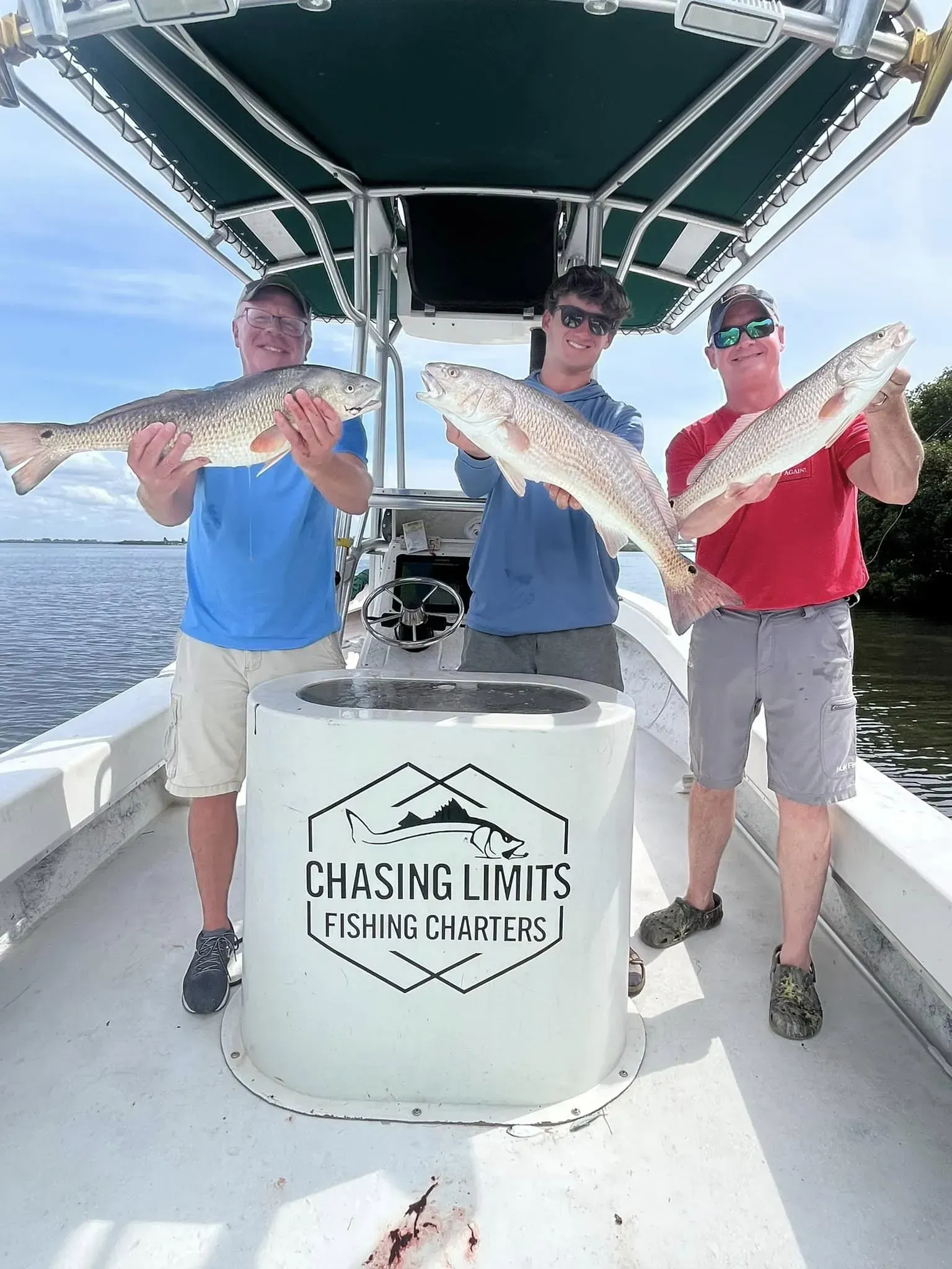 Three men are standing on a boat holding fish.