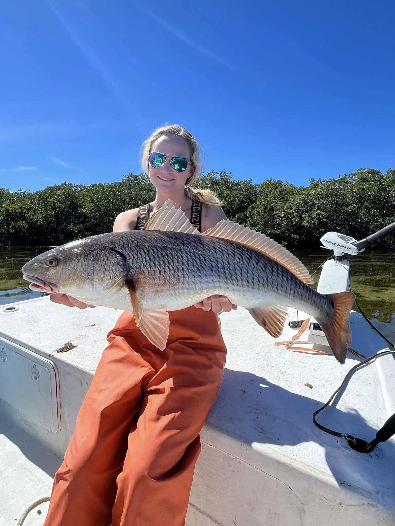 A woman is sitting on a boat holding a large fish.