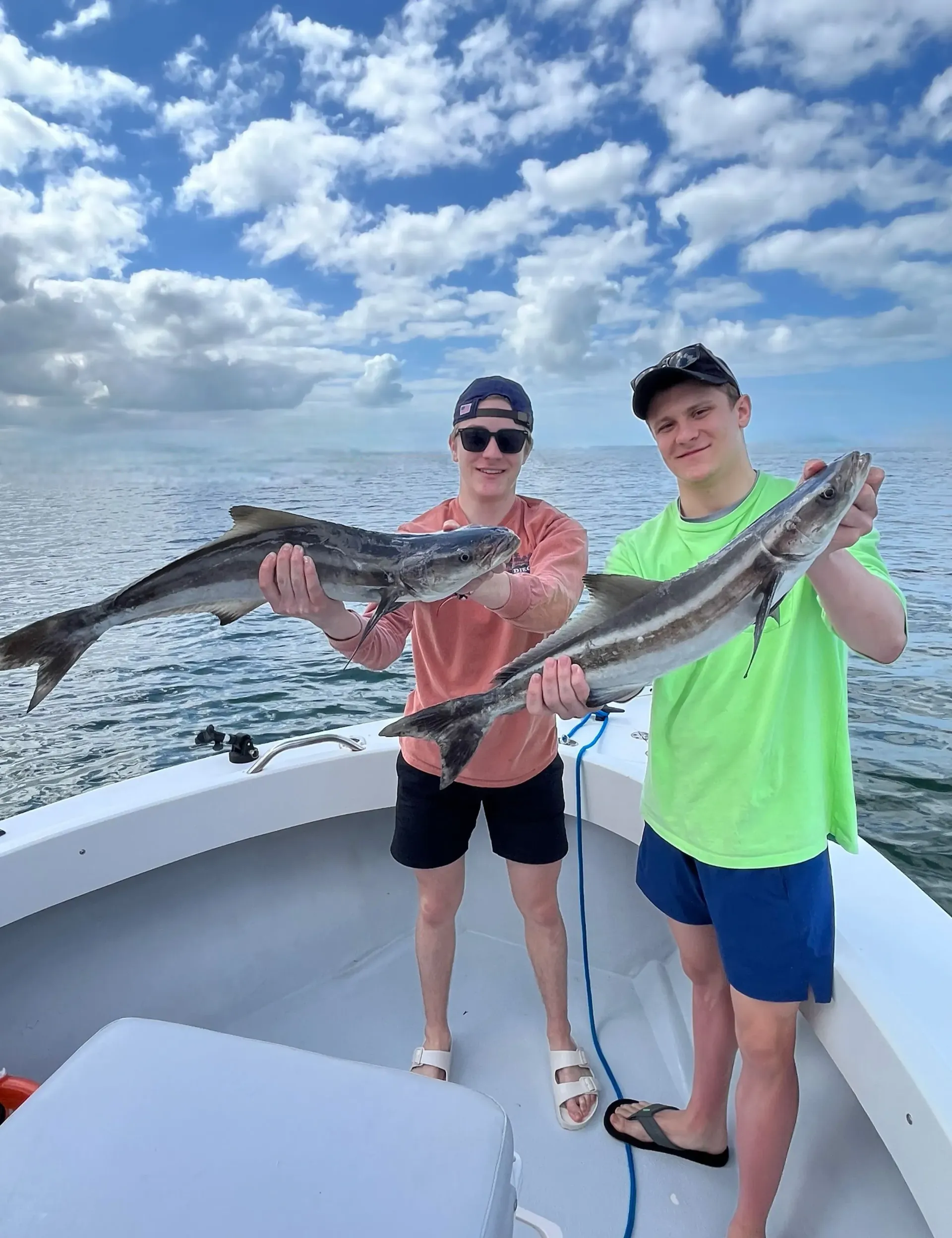 Two men are holding fish on a boat in the ocean.
