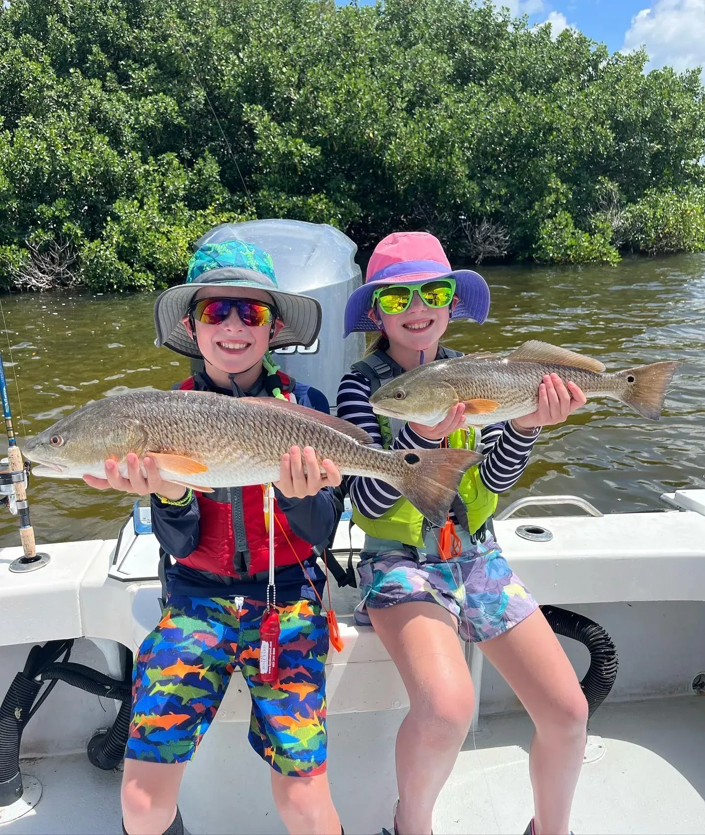 A boy and a girl are sitting on a boat holding fish.