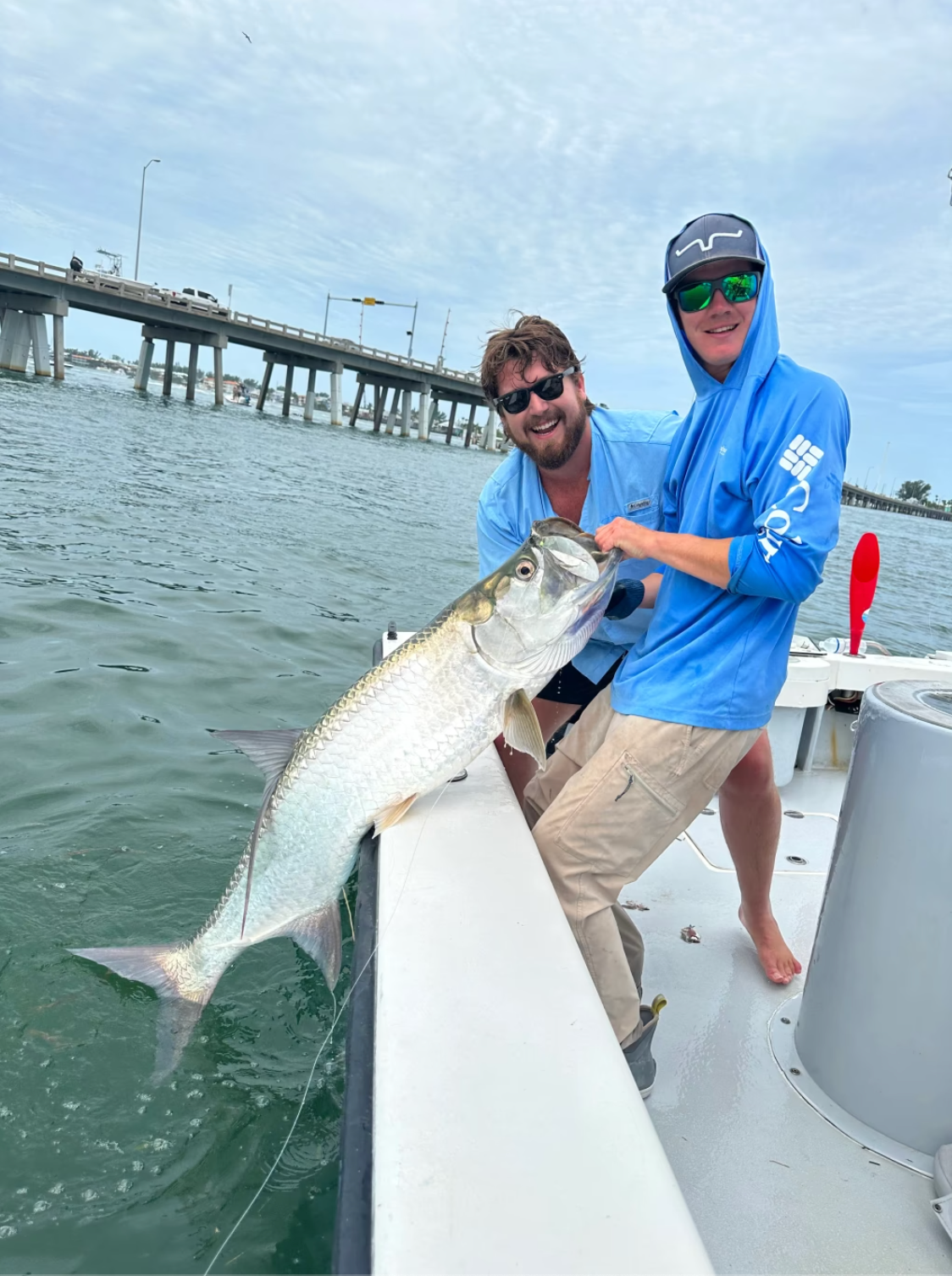 Two men are standing on a boat holding a large fish.
