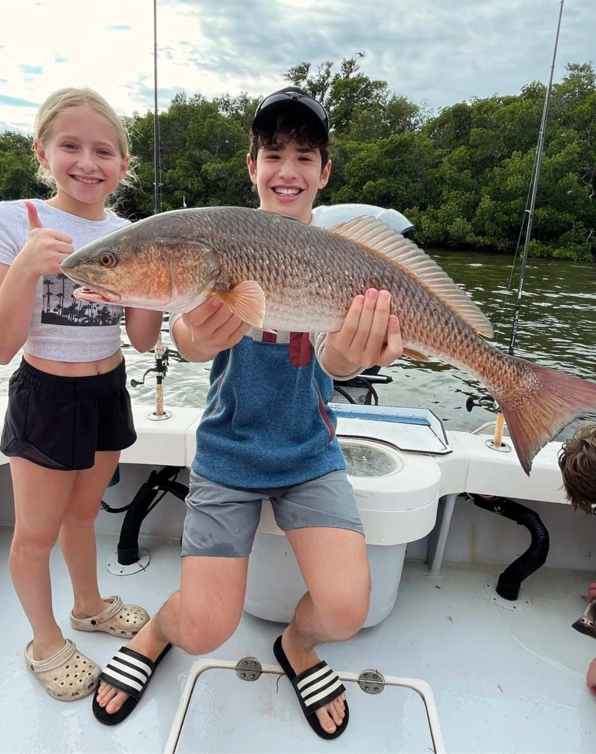 A boy and a girl are holding a large fish on a boat.