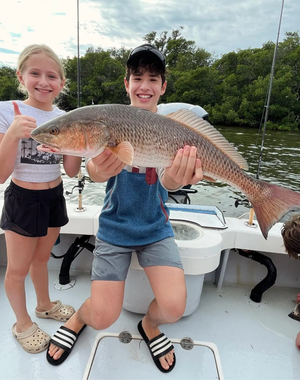 A boy and a girl are holding a large fish on a boat.