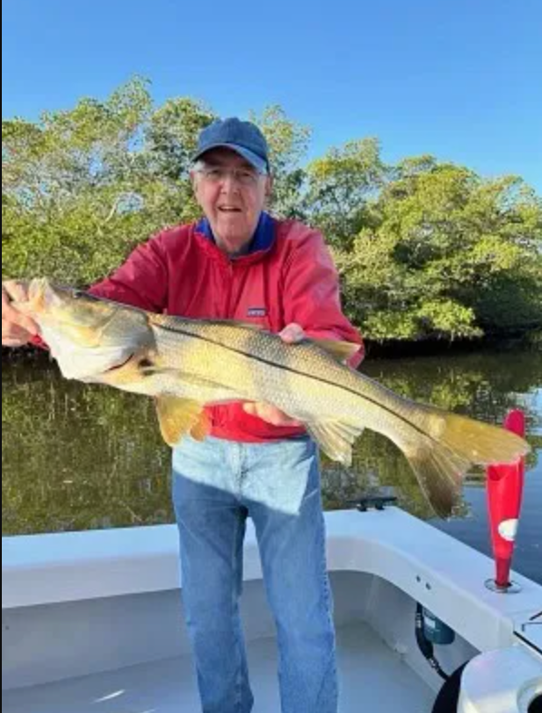 A man in a red jacket is holding a large fish on a boat.