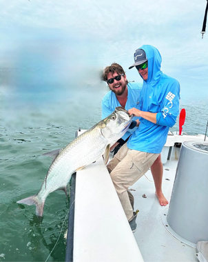 Two men are standing on a boat holding a large fish.