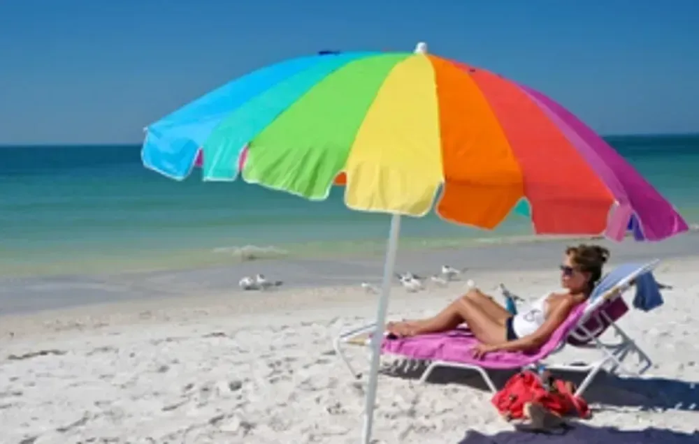 A woman sits under a colorful umbrella on the beach