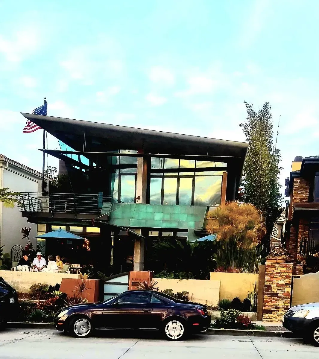 Modern house with copper facade, angled roof, and flag; parked cars in front.