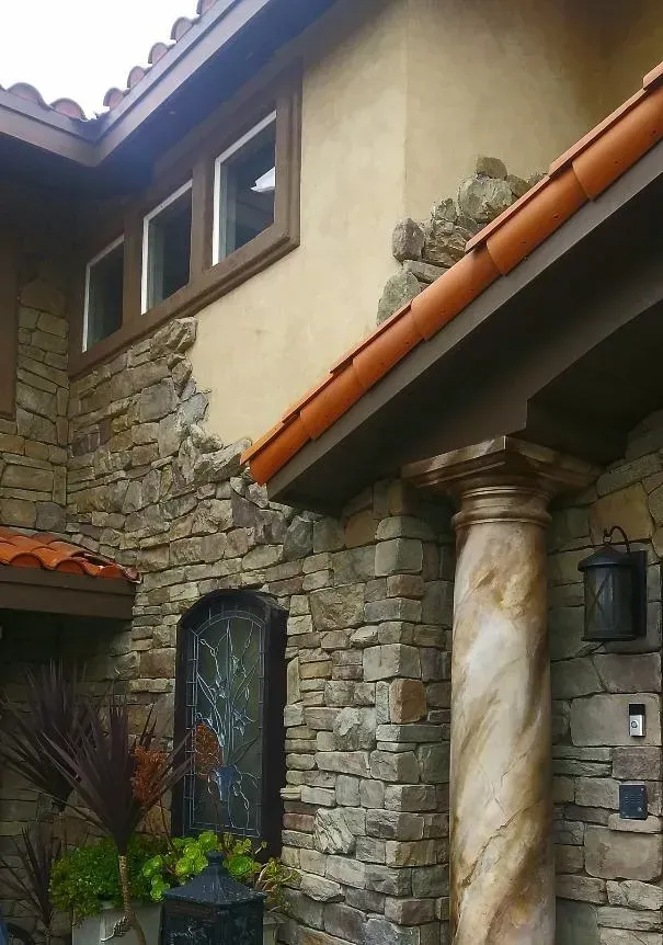Stone facade of a building with a decorative column, arched doorway, and windows under a clay tile roof.