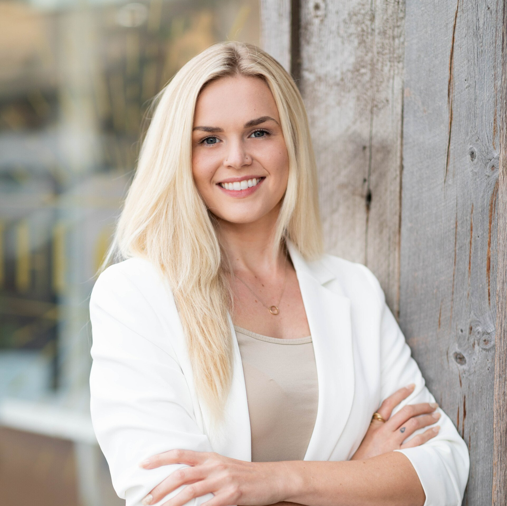 A woman is leaning against a wooden wall with her arms crossed and smiling.