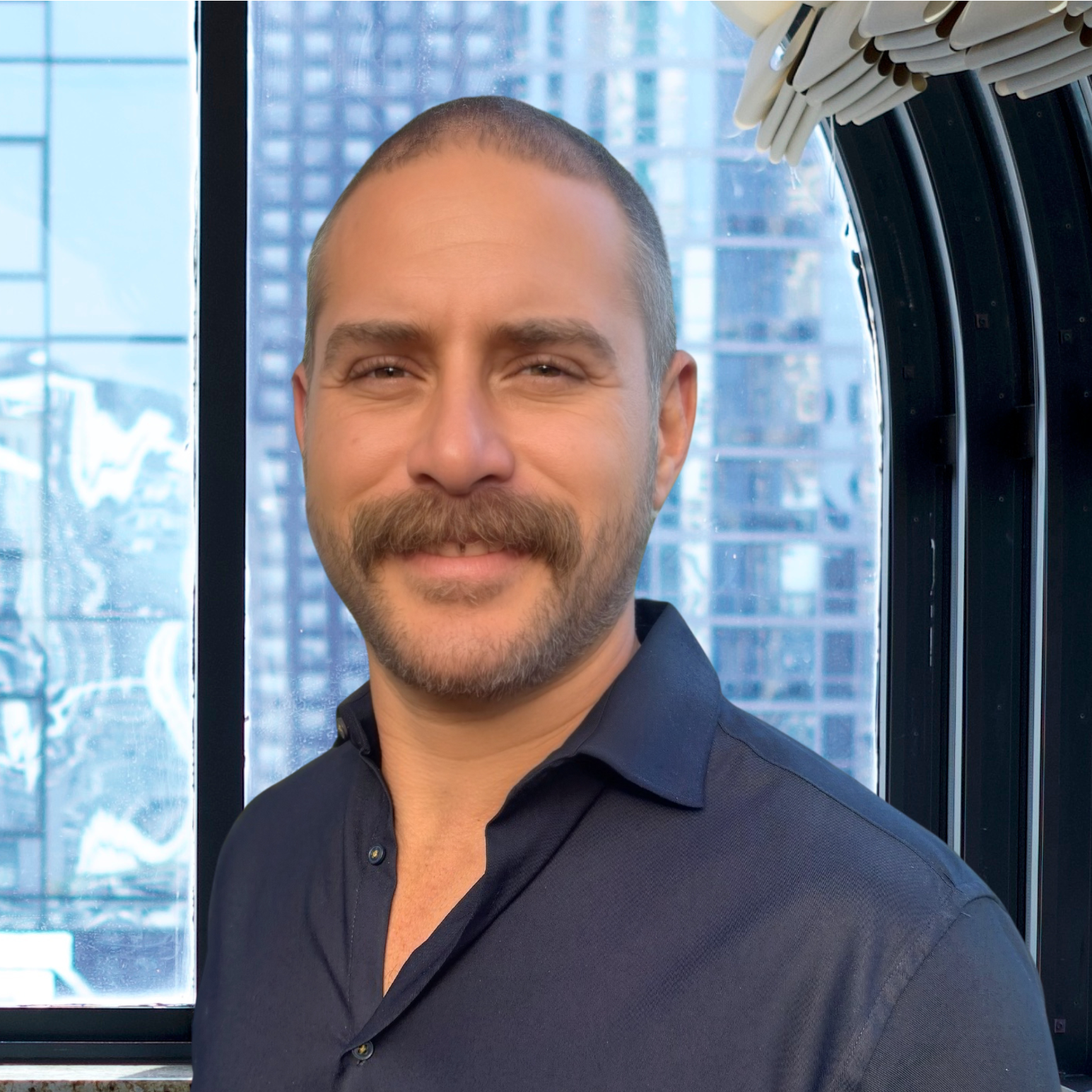 A man with a mustache is smiling in front of a window