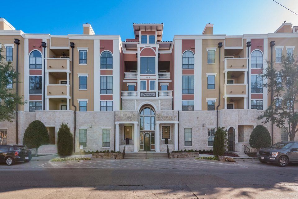 A red car is parked in front of a large apartment building.